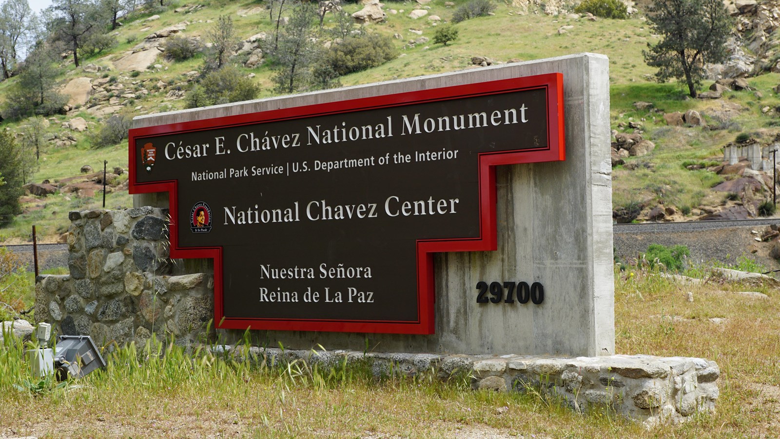 A sign in white letters with a black background and red trim against a cement wall.