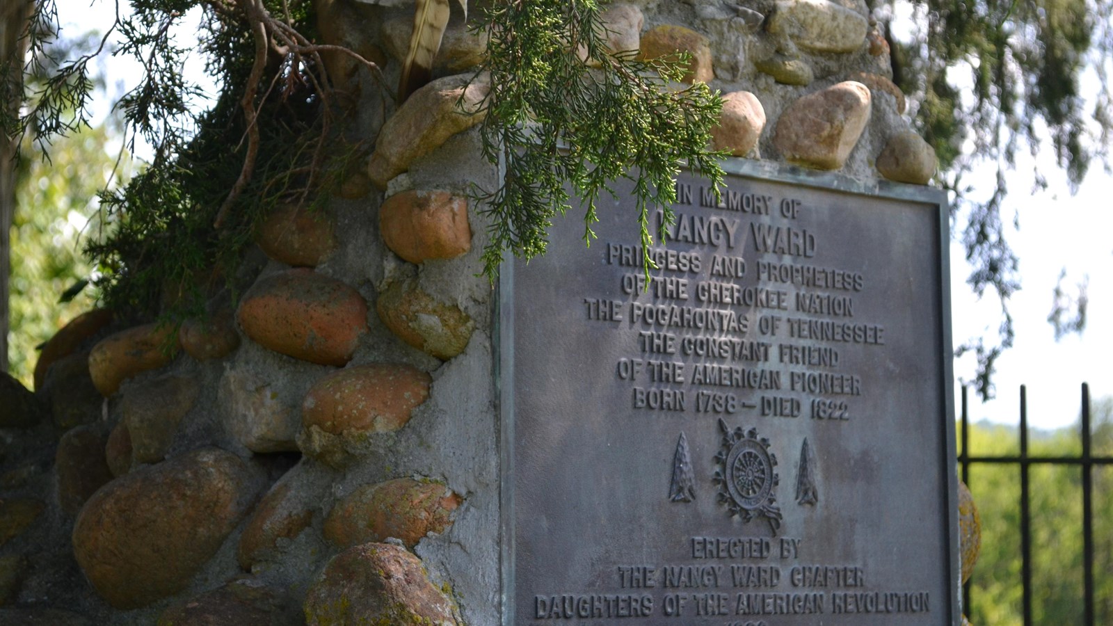 A monument made of stone surrounded by greenery with a metal plaque on front in memory of Nancy Ward