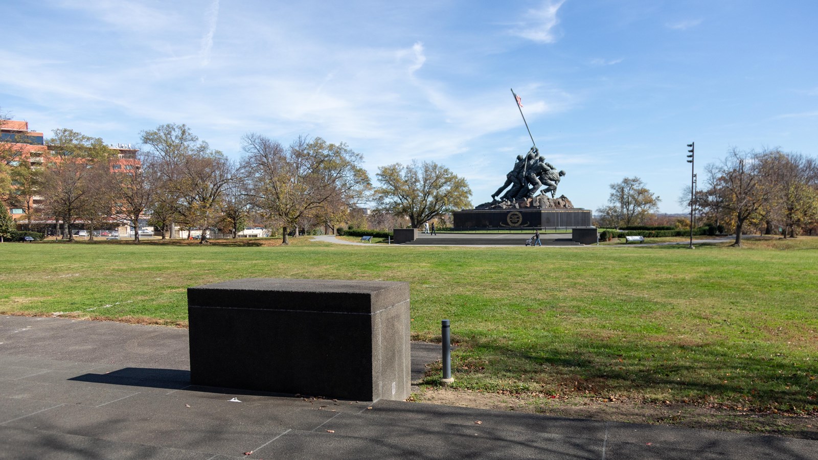 A short stone bench in front of a statue of a group of marines holding up the american flag. 