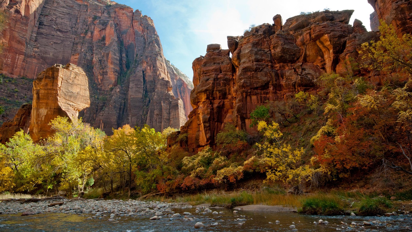 A redrock sandstone formation under blue skies, with a clear river running in front of it.