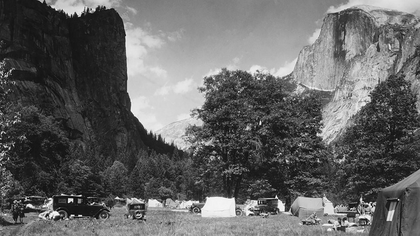 Black and White photo with tents and old cars set up in meadow