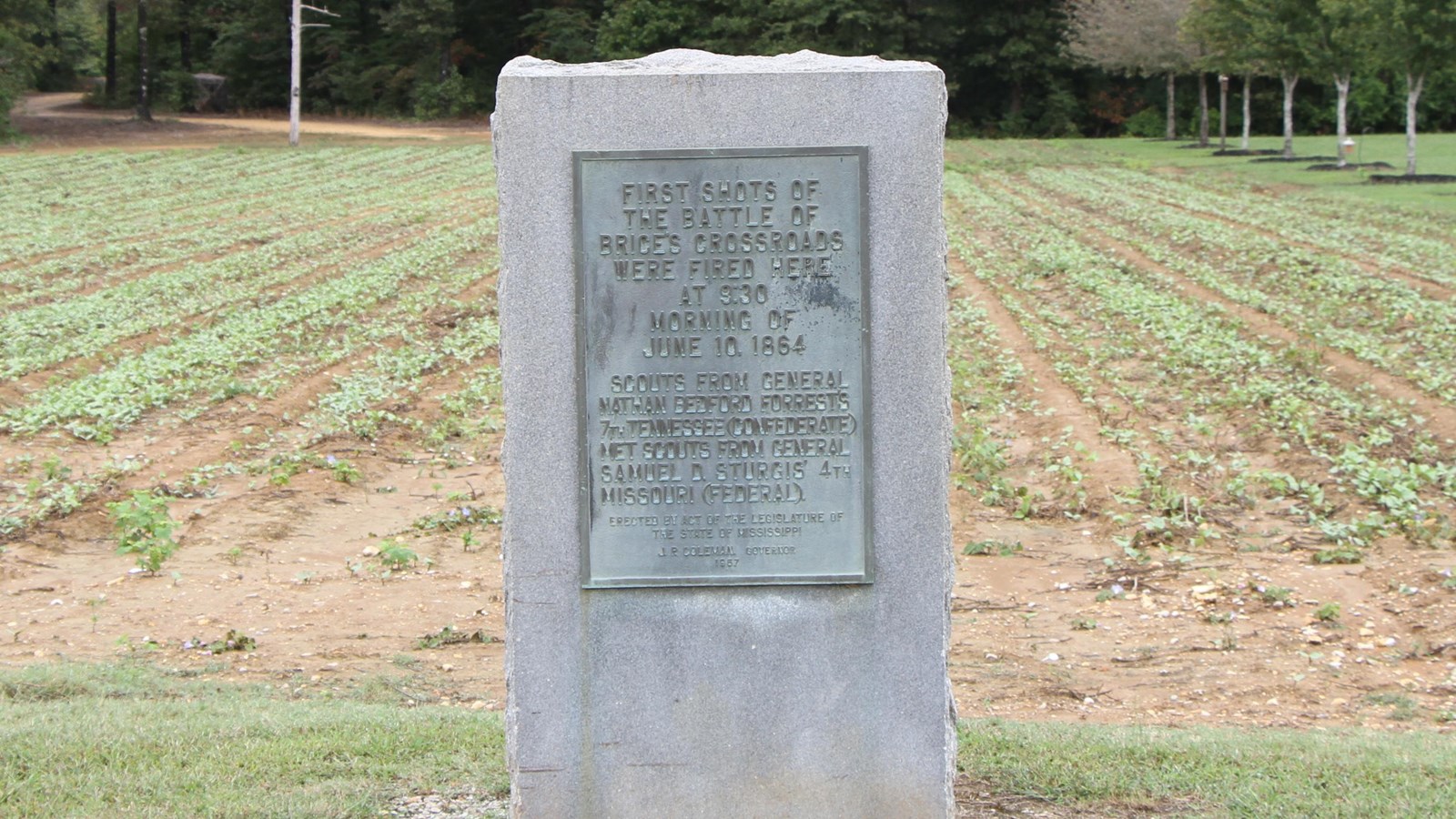 Granite marker about 4 feet tall and rectangular in shape. Brass plate with first shot info on front