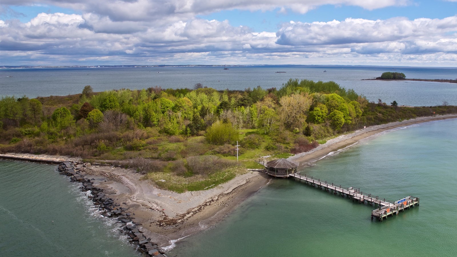 Birds eye view of a rectangular island sitting in blue green water. A t shaped pier extends out