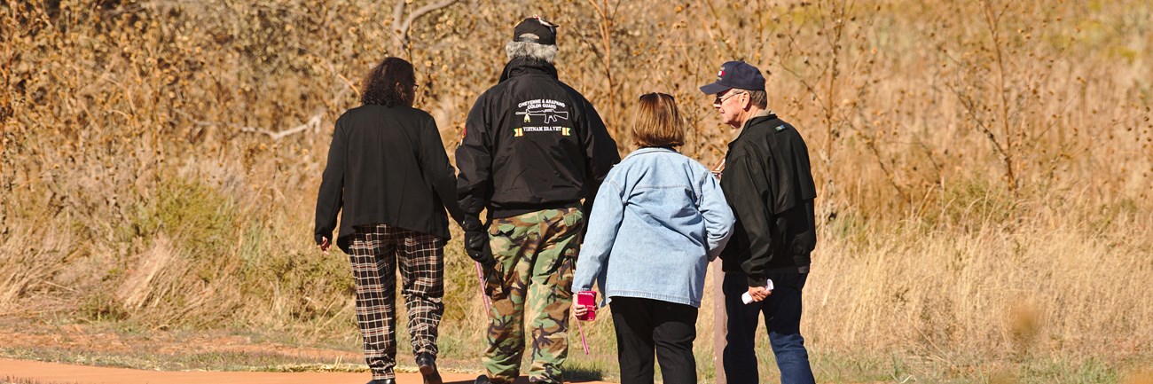 Four people walking a paved trail through a grasslands