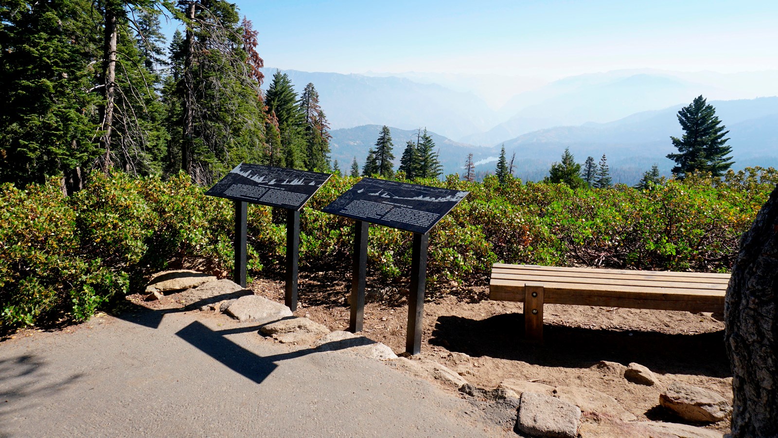 black metal panels stand in front of an asphalt path. Behind it are bushes and mountains