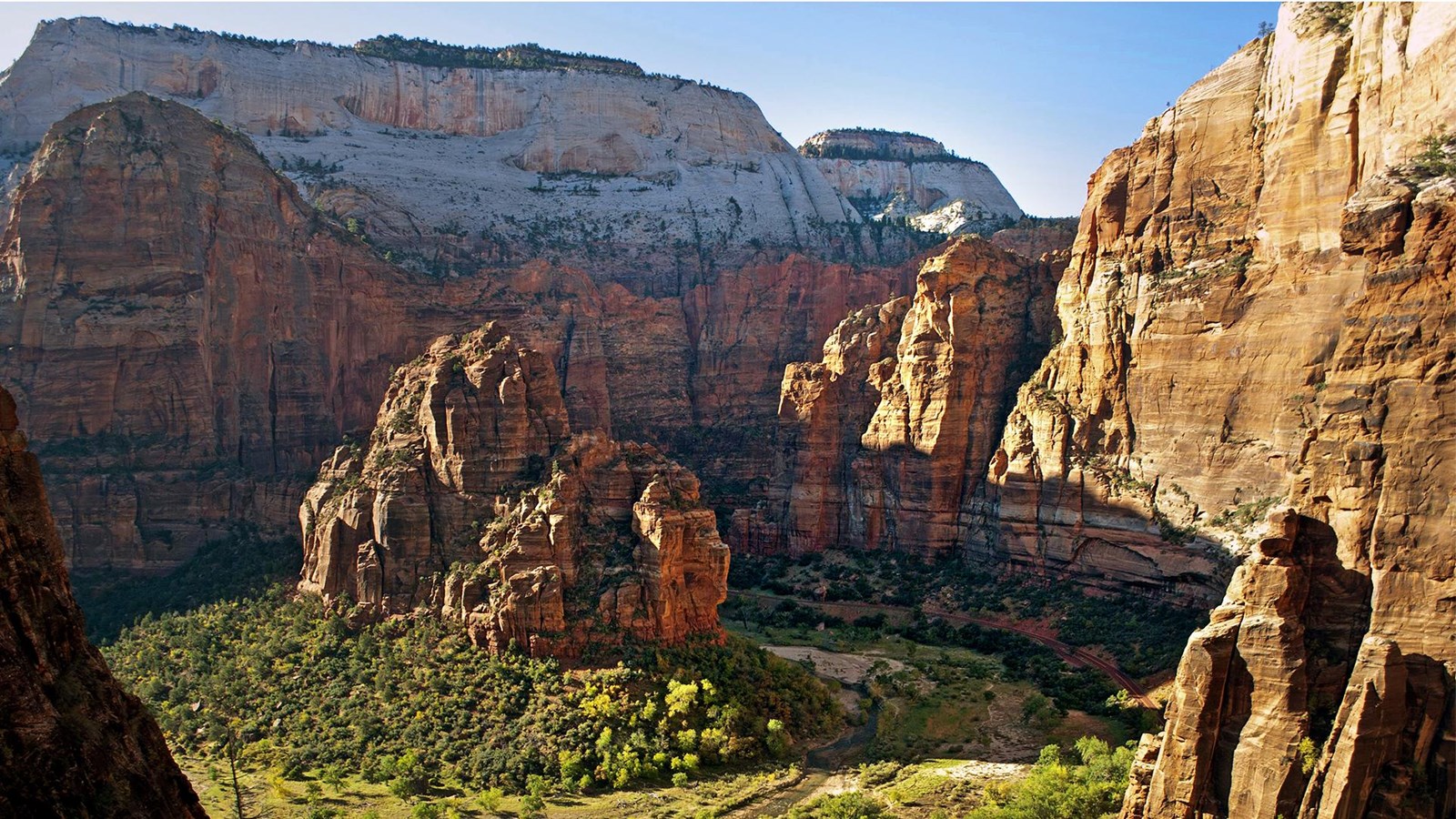 A red road follows the path of a river around a large, red, sandstone mountain.