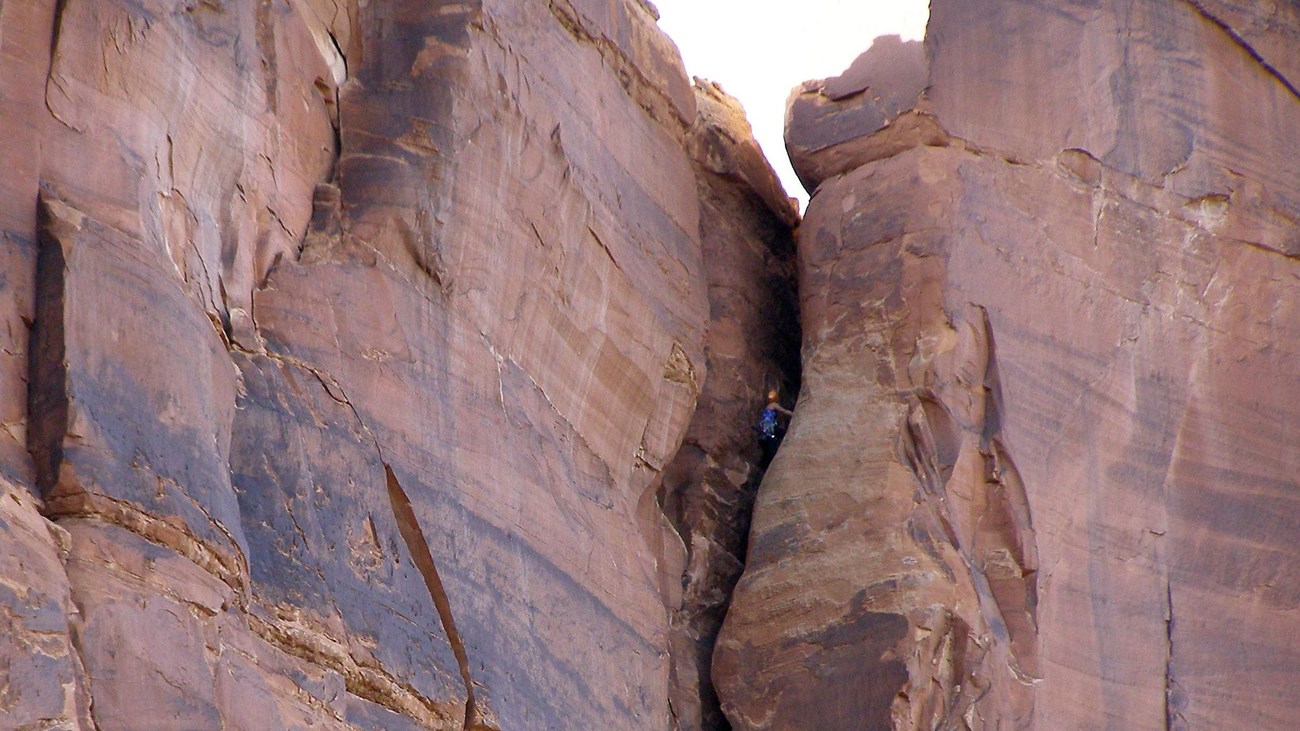 rock climber with red helmet perched in red sandstone crack