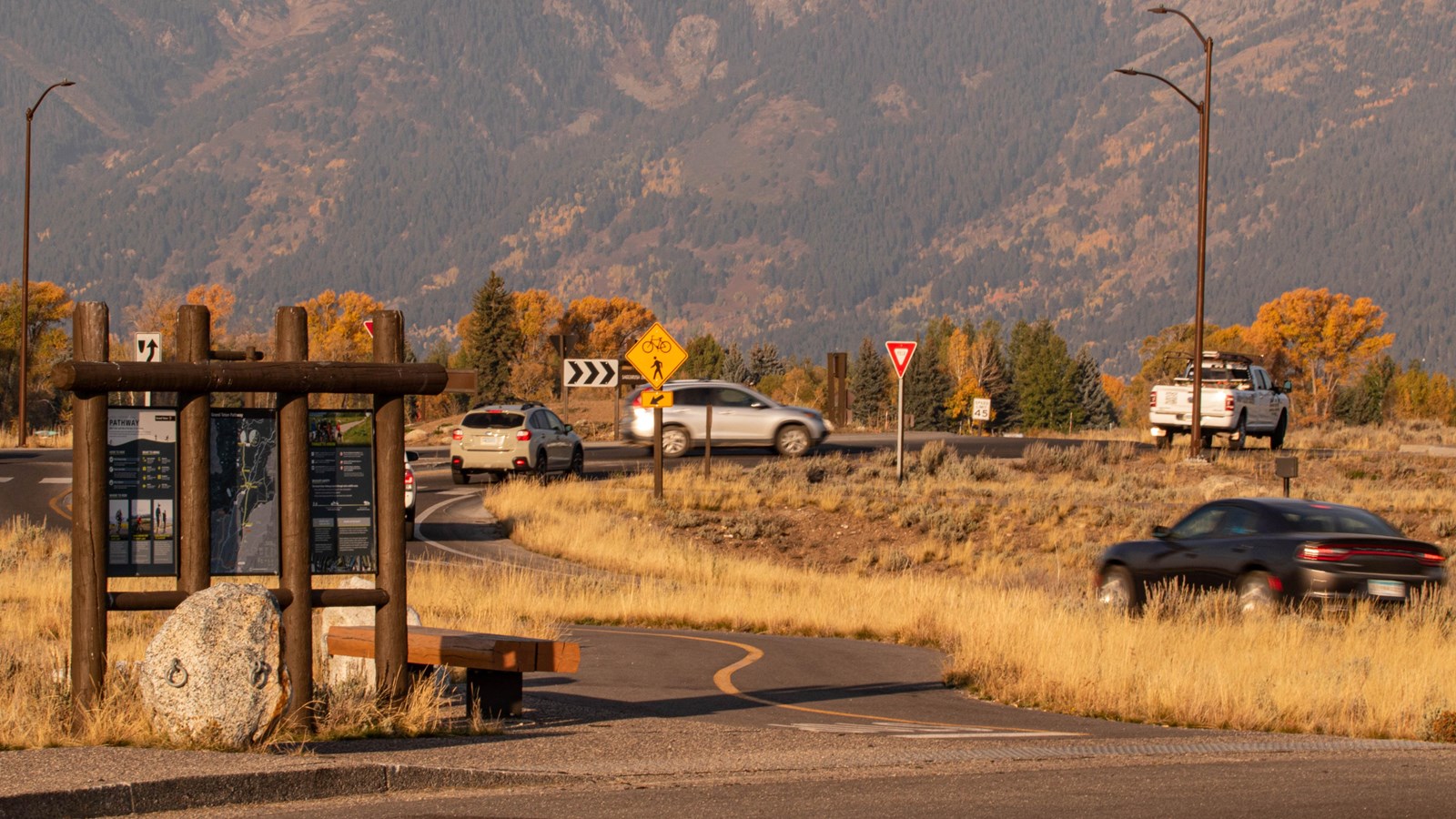 A three panel sign in the foreground with a roundabout and moving card in the background.