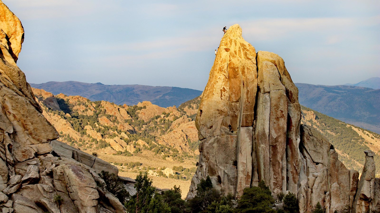Climbers can be seen ascending the impressive granite spire as fading sunlight grazes the land.