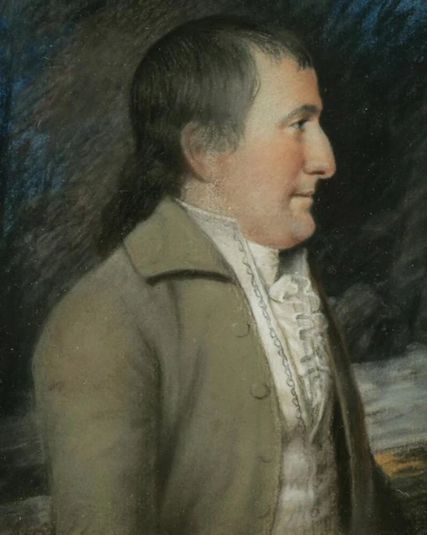 A man in profile with a drab colored, well-fitting suit.