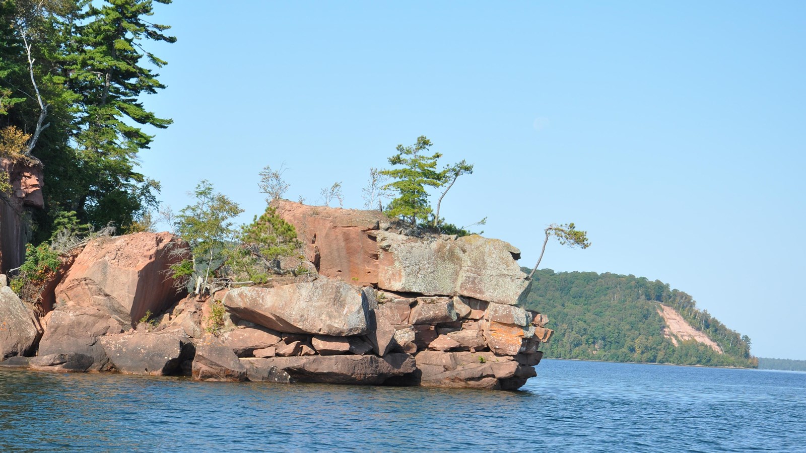 A rocky ledge sticking out of the water with tree covered cliffs in the background. 
