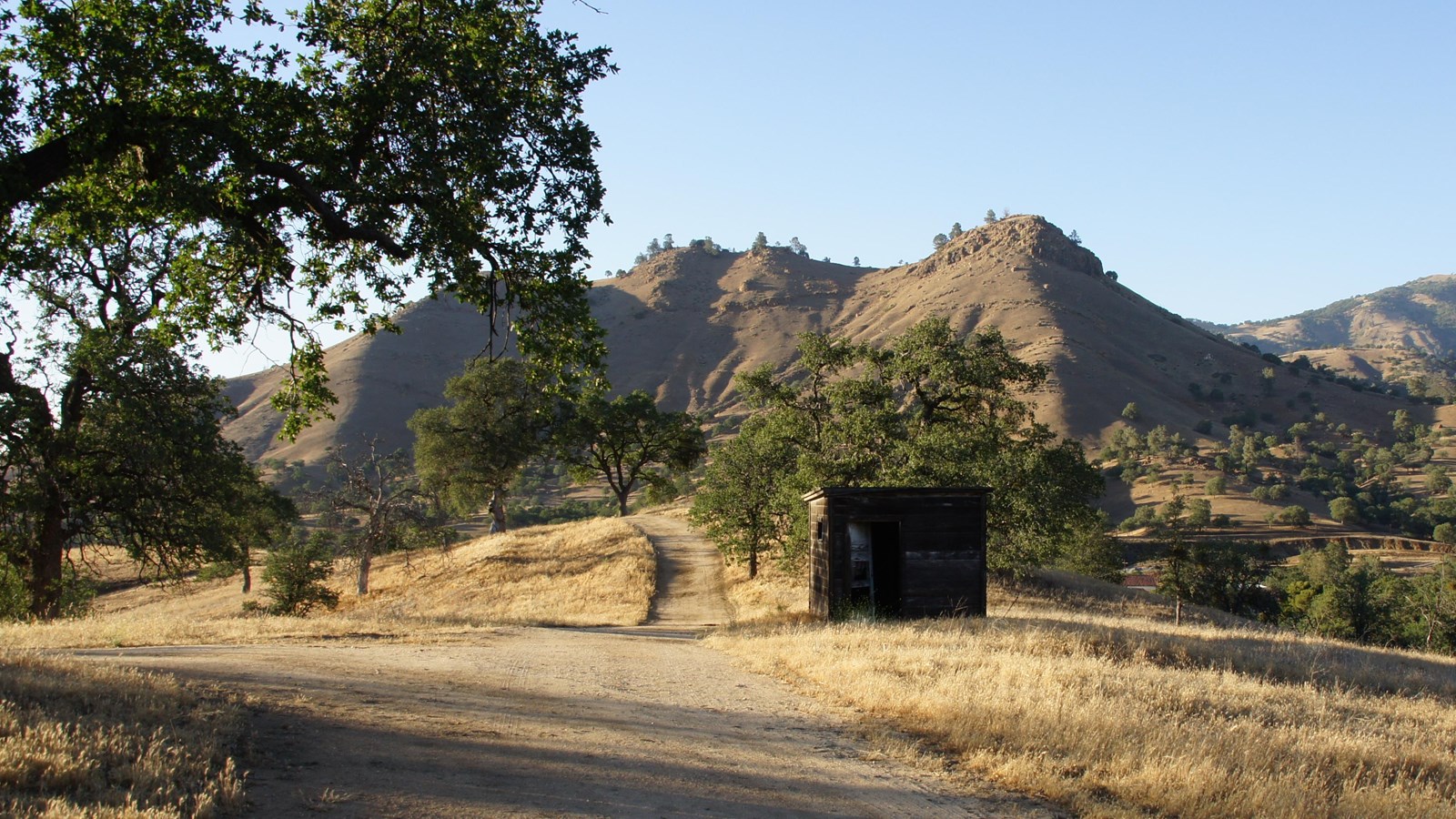 Three rounded peaks can be seen in the distance. Dry grasses and a dirt path in the foreground.