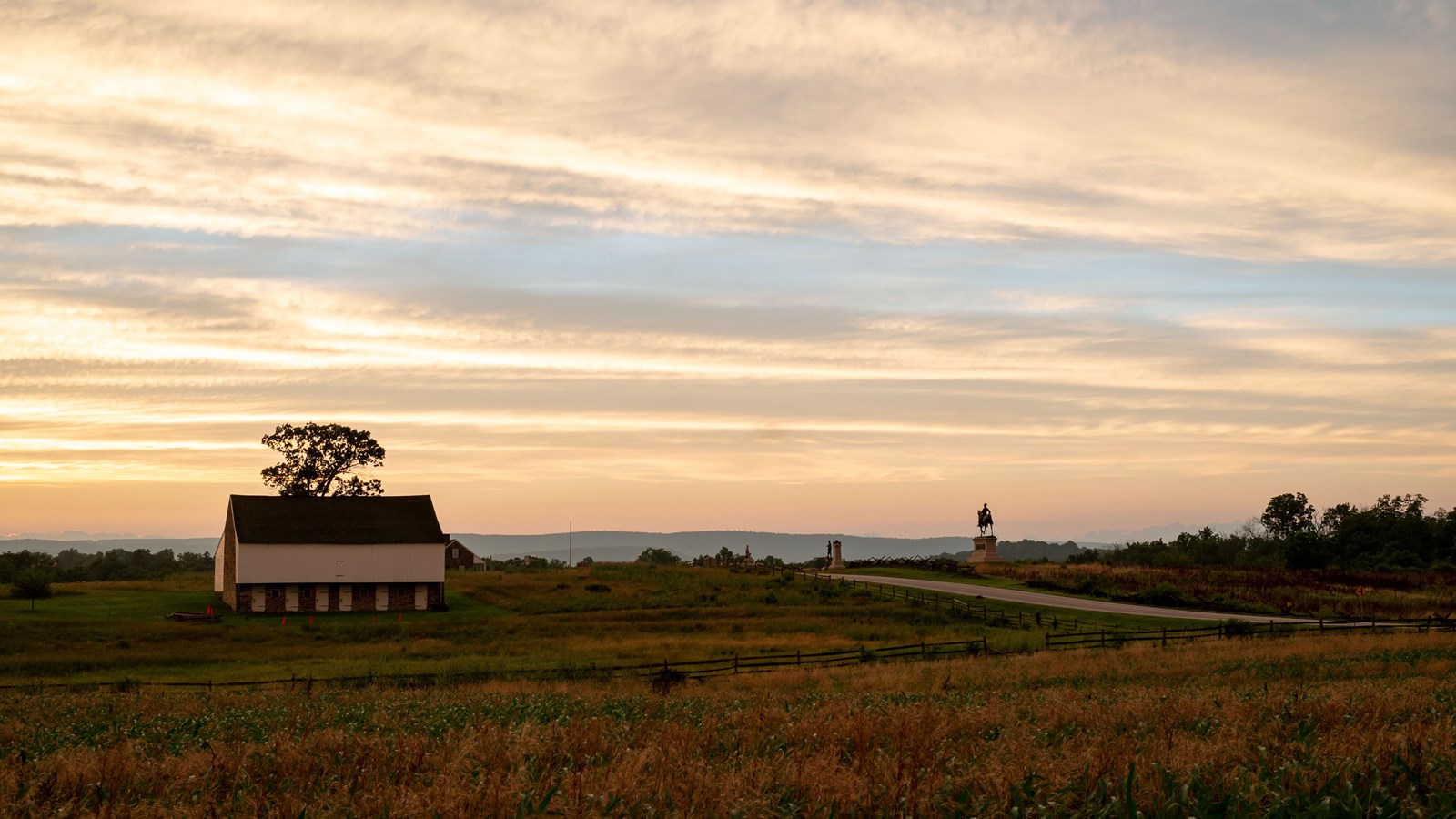 A white and brick bank barn sitting on a ridgeline with trees scattered in the green fields.