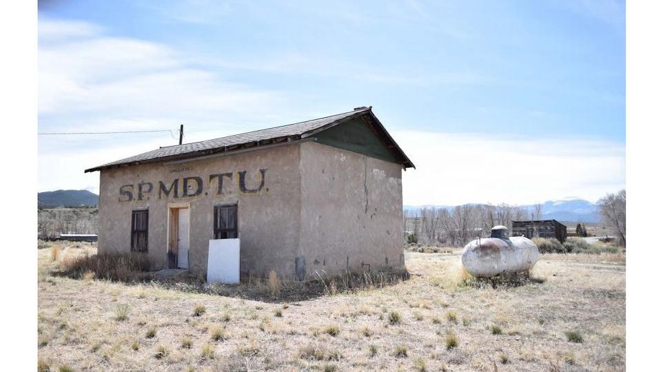 single story rectangular building with one door and two windows in a plain landscape