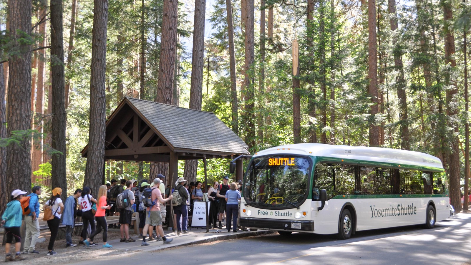 Shuttle bus at stop and covered shelter with lots of people waiting to board.