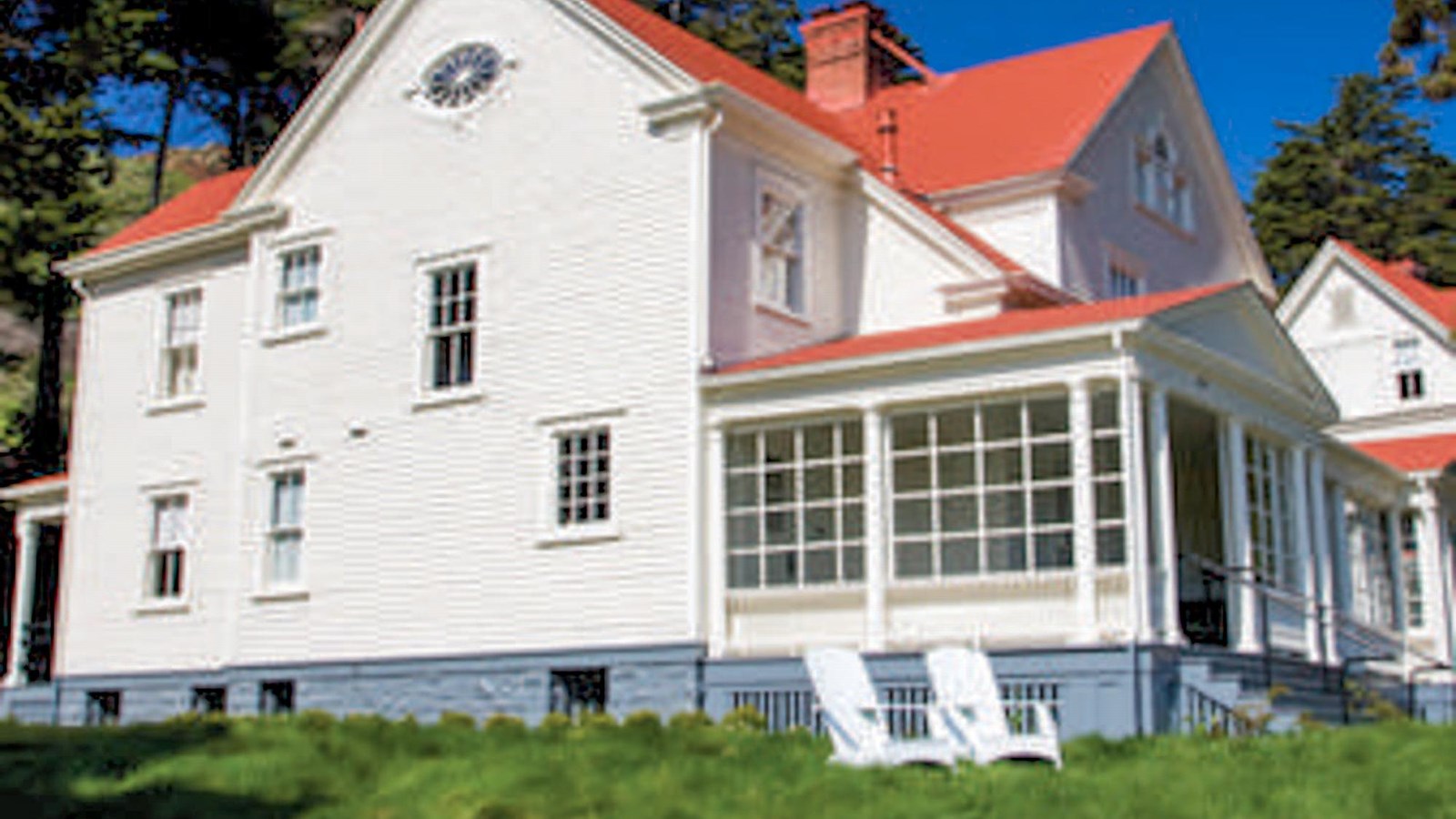 Colored photo of an officer\'s house with a red roof and white siding. In front are two white chairs.