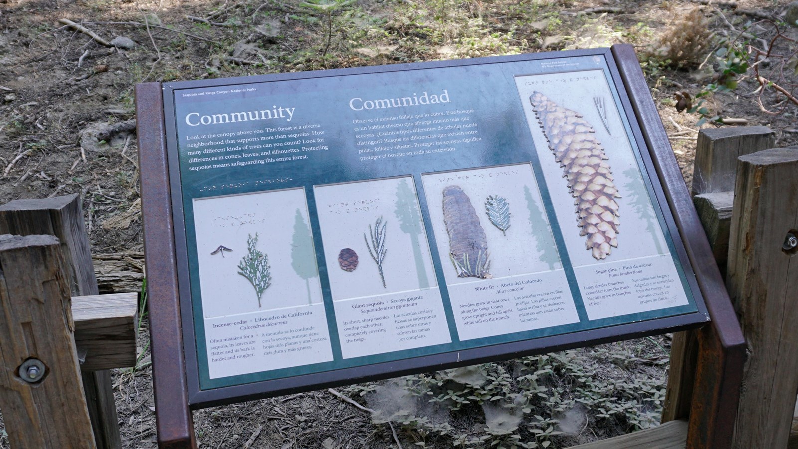 A metal panel with images and text stands in front of a wooden fence.