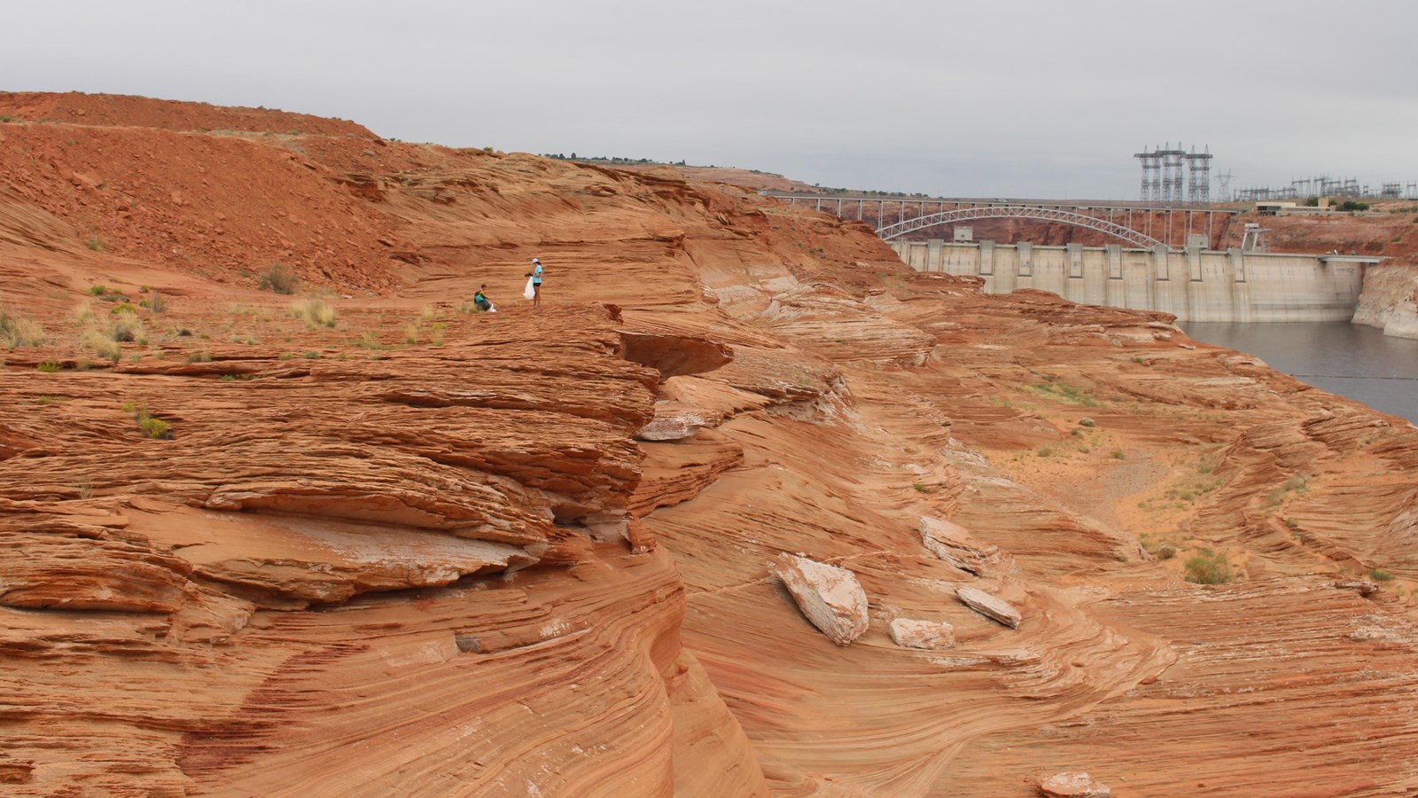 people in the distance on swirly sandstone hills in front of a large concrete dam
