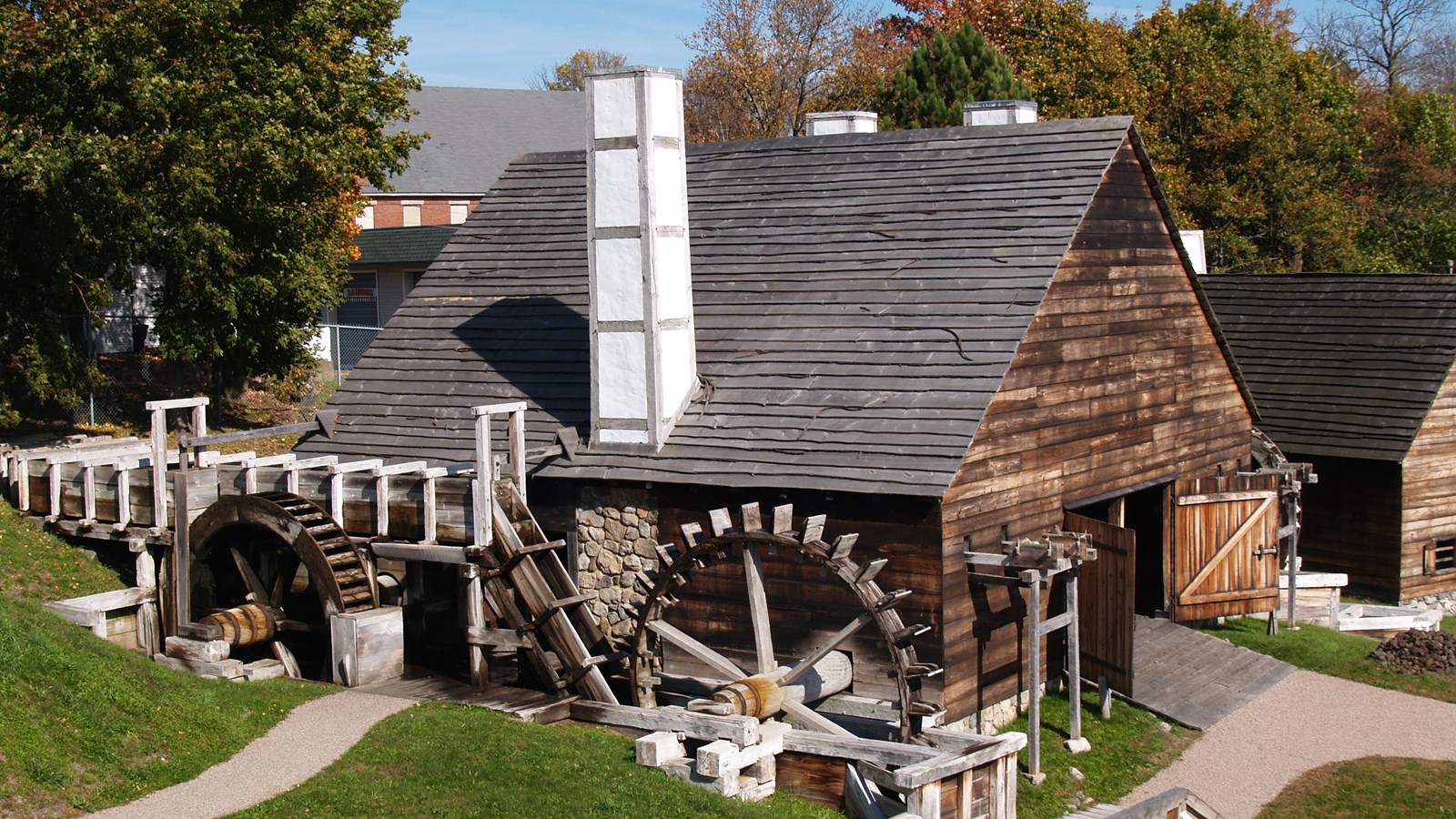 A wood cladded barn shaped structure with waterwheels and chimneys on either side
