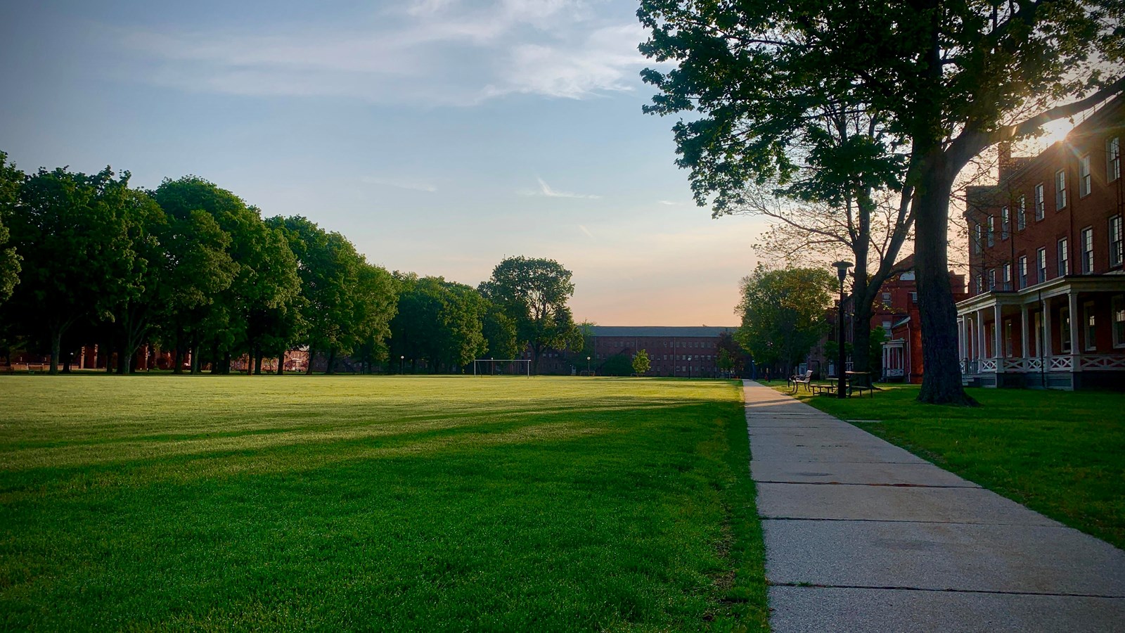 The sun rises over the grounds of the Armory, highlighting buildings on the right and the green 