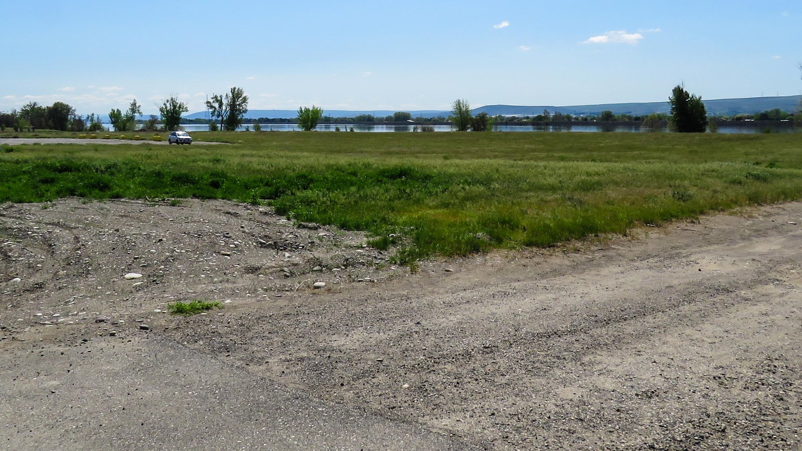 Color photograph of an empty field with an expanse of green behind it with no visible buildings near