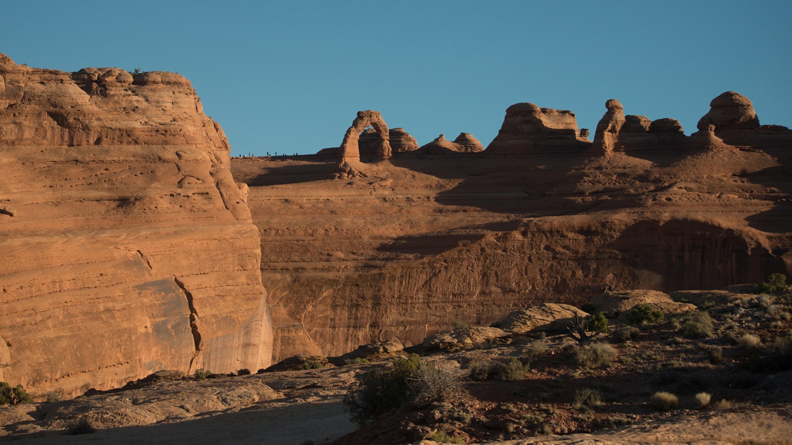 A free-standing sandstone arch and other rock features, viewed across a canyon.