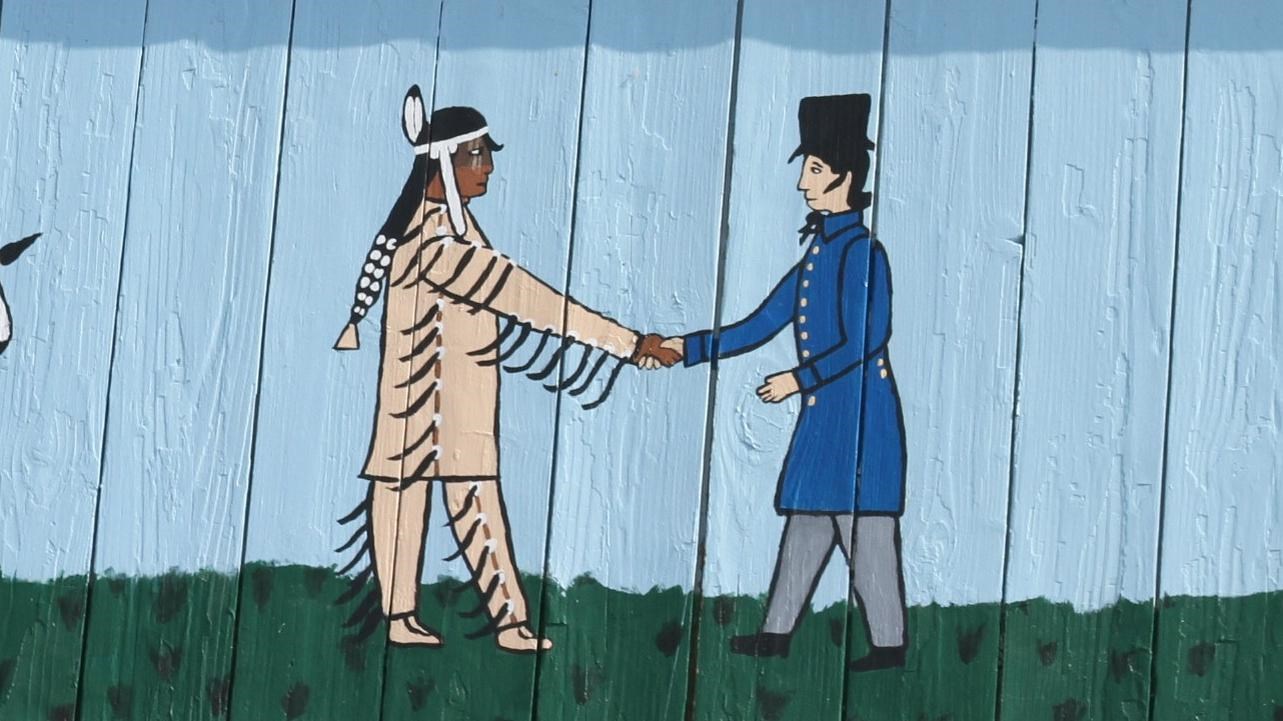 Mural, two men shaking hands in center, three men watching on each side. Eagle watching over all.