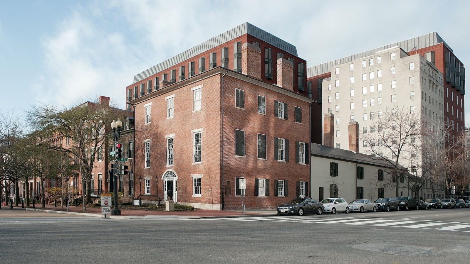 View of a three story red brick building and a busy city street with several cars parked nearby. 