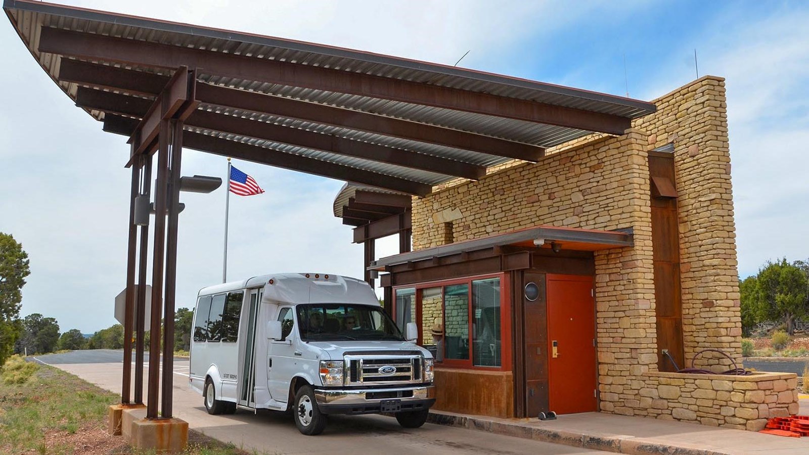 A tour van is purchasing a pass from a park ranger in a yellow brick entrance lane building