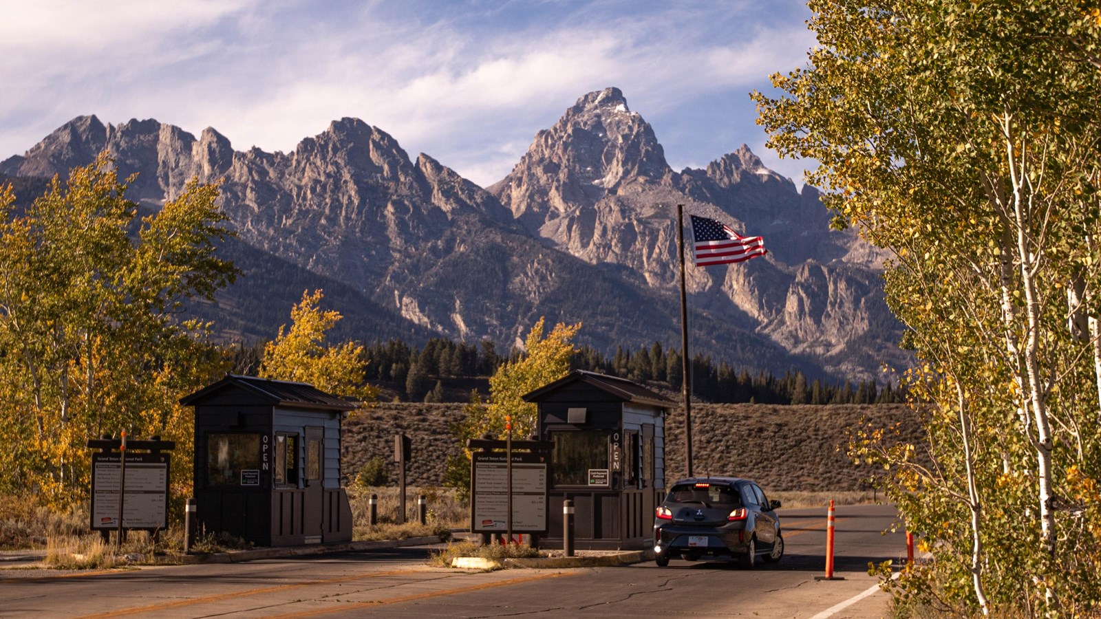 Two entrance booths with a car going through and the Teton range in the background.