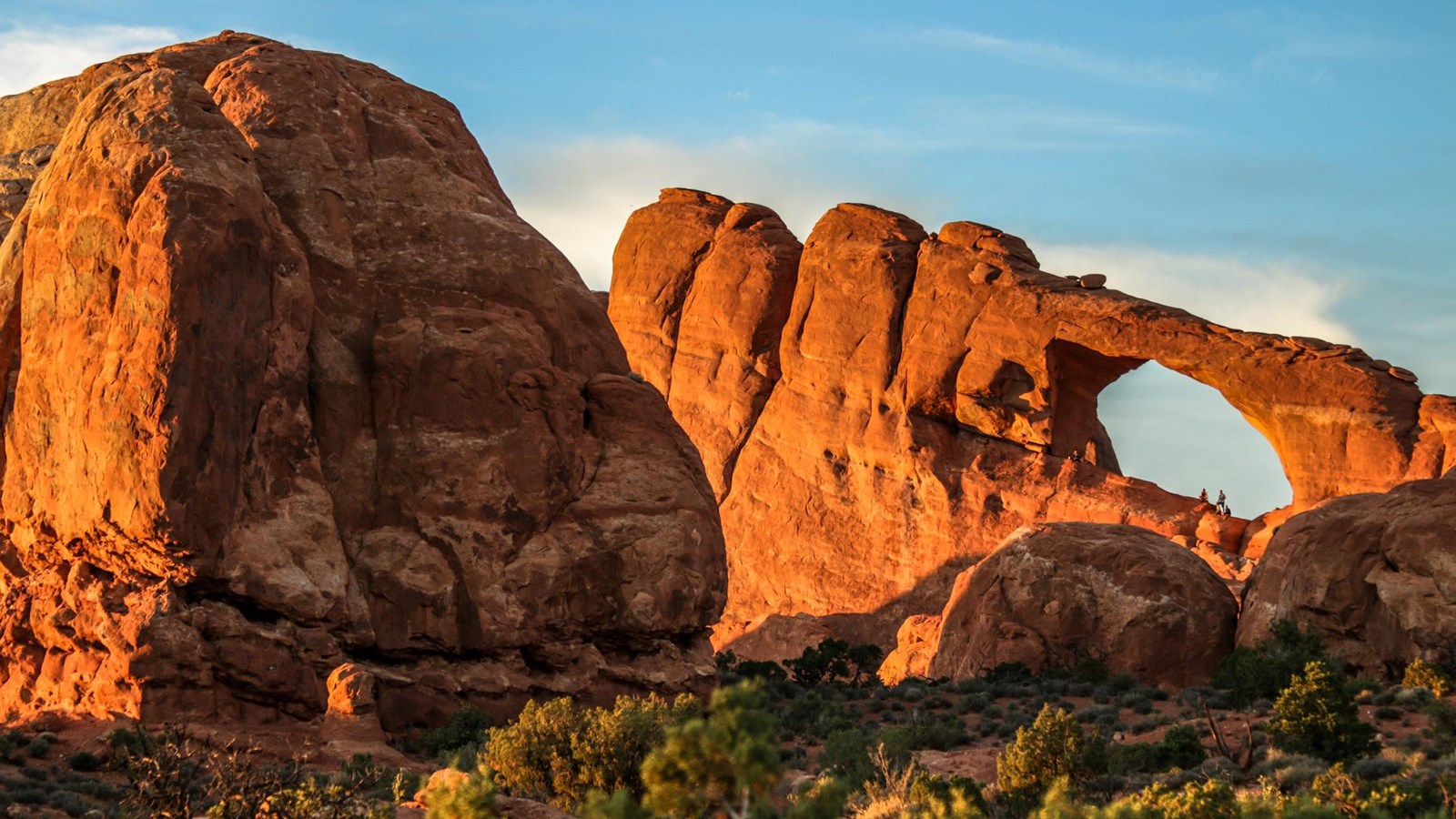A large sandstone arch is visible at sunset
