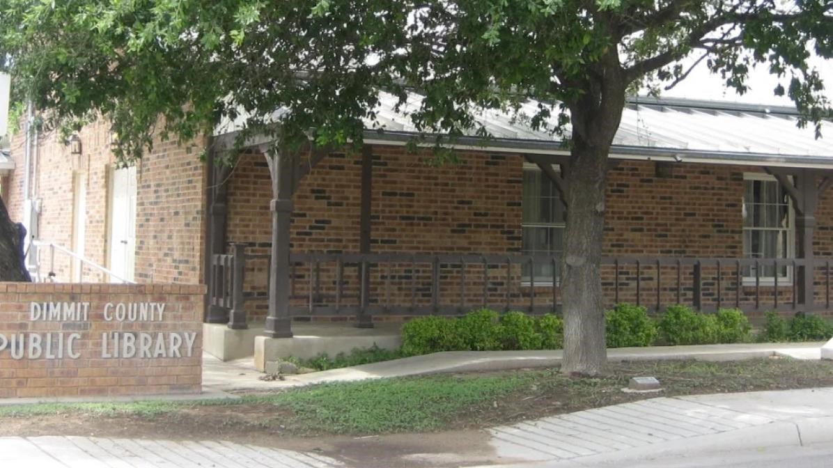 A brick building with a sign and trees in front blocking the roof