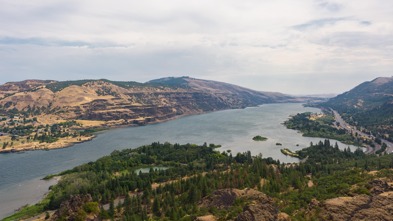 An wide river stretches through a heavily forested gorge under a cloudy sky.