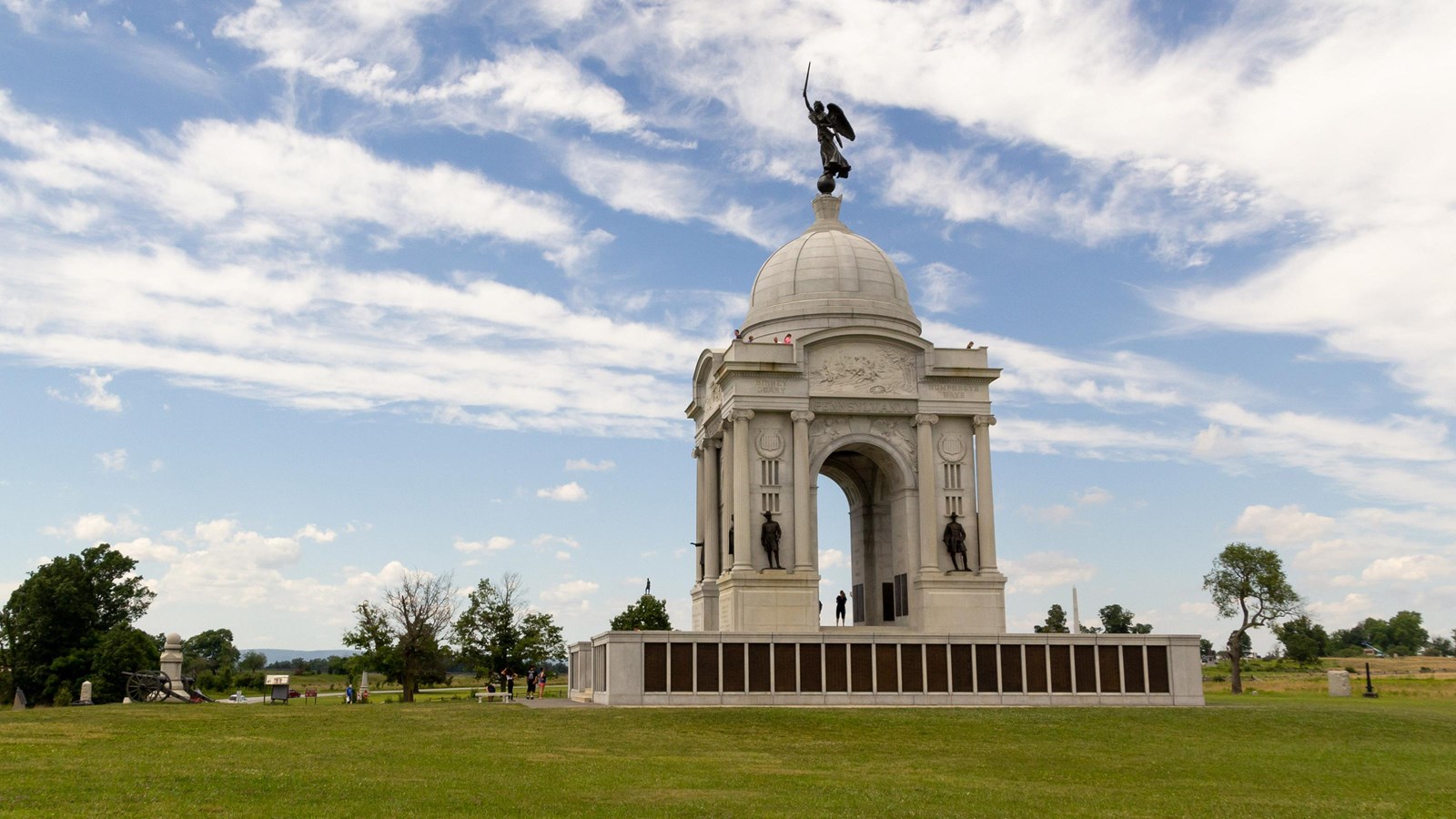 A large marble monument sitting on a ridgeline, near a farm field