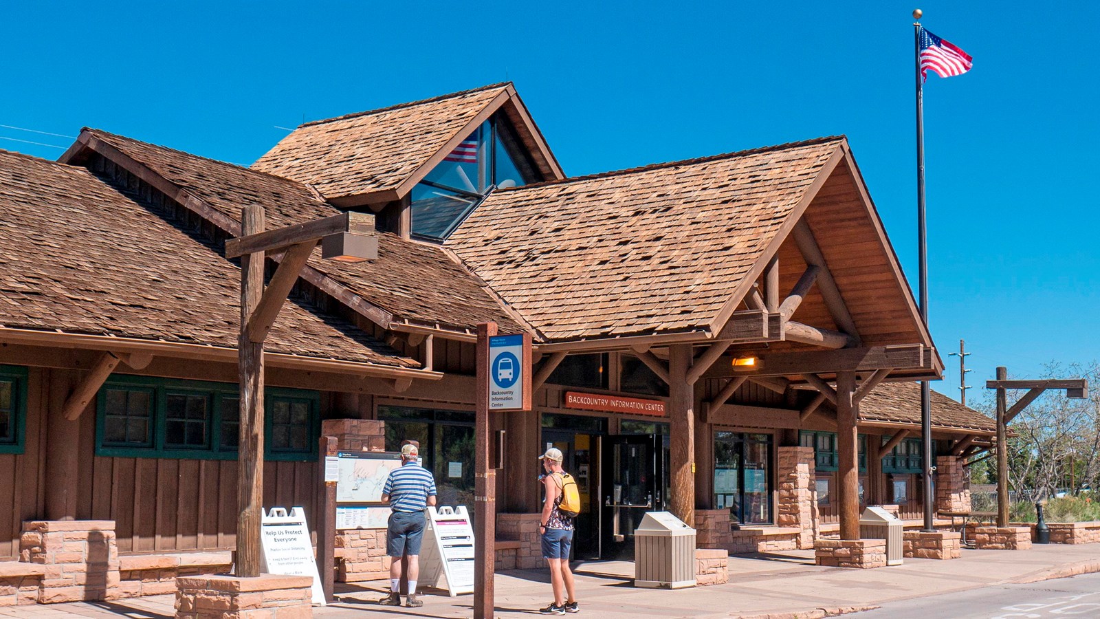 A brown wooden and stone building with a large peaked roof, glass windows, and glass doors.