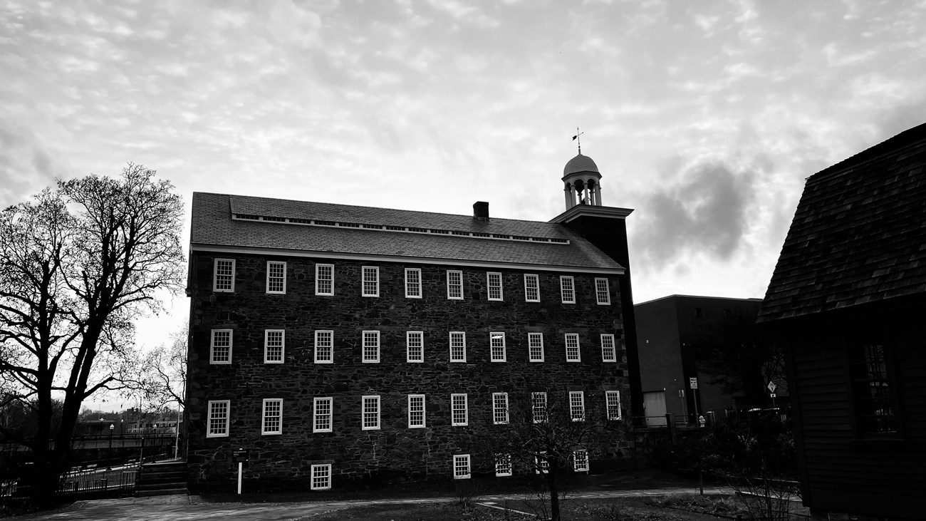 Picture of large 4 story stone mill with bell tower. Black and white photograph