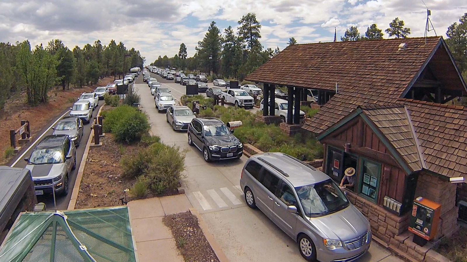 Multiple lines of cars wait in line at a two peaked wooden building that covers the lanes. 