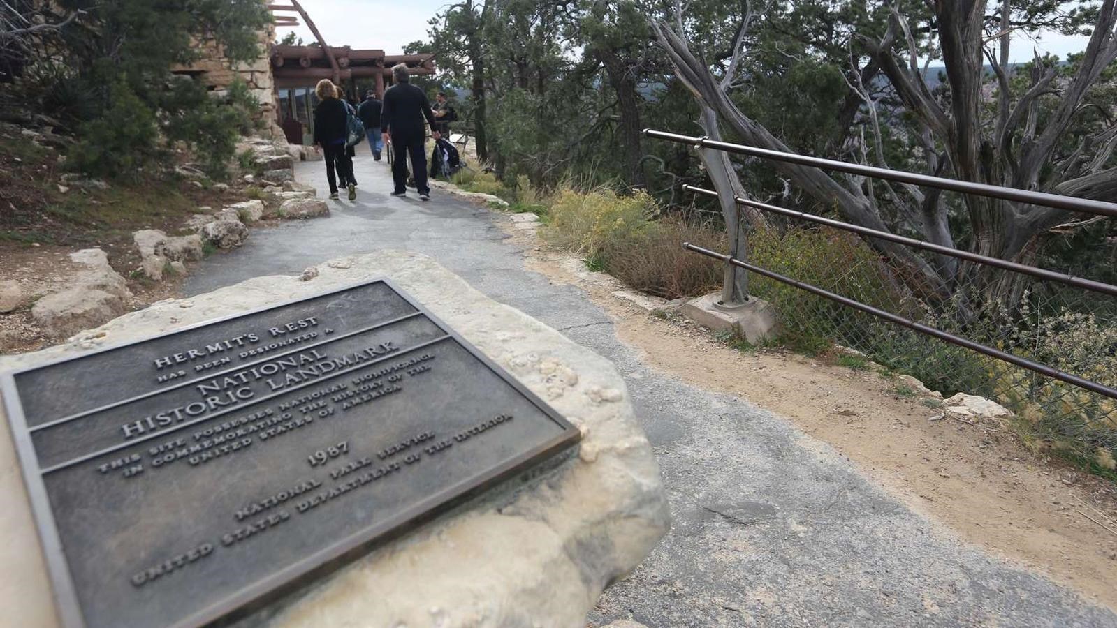 A bronze plaque rests on top of a limestone column in the middle of a path.