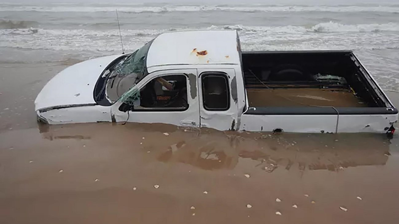 A white truck stuck in wet sand on a beach.