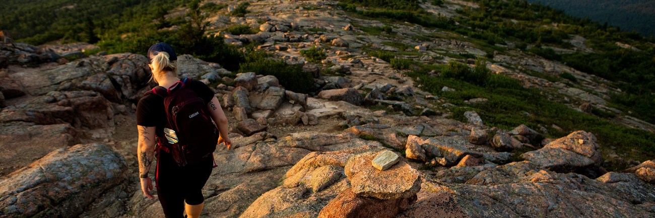 Visitor hikes down granite trail marked with cairns