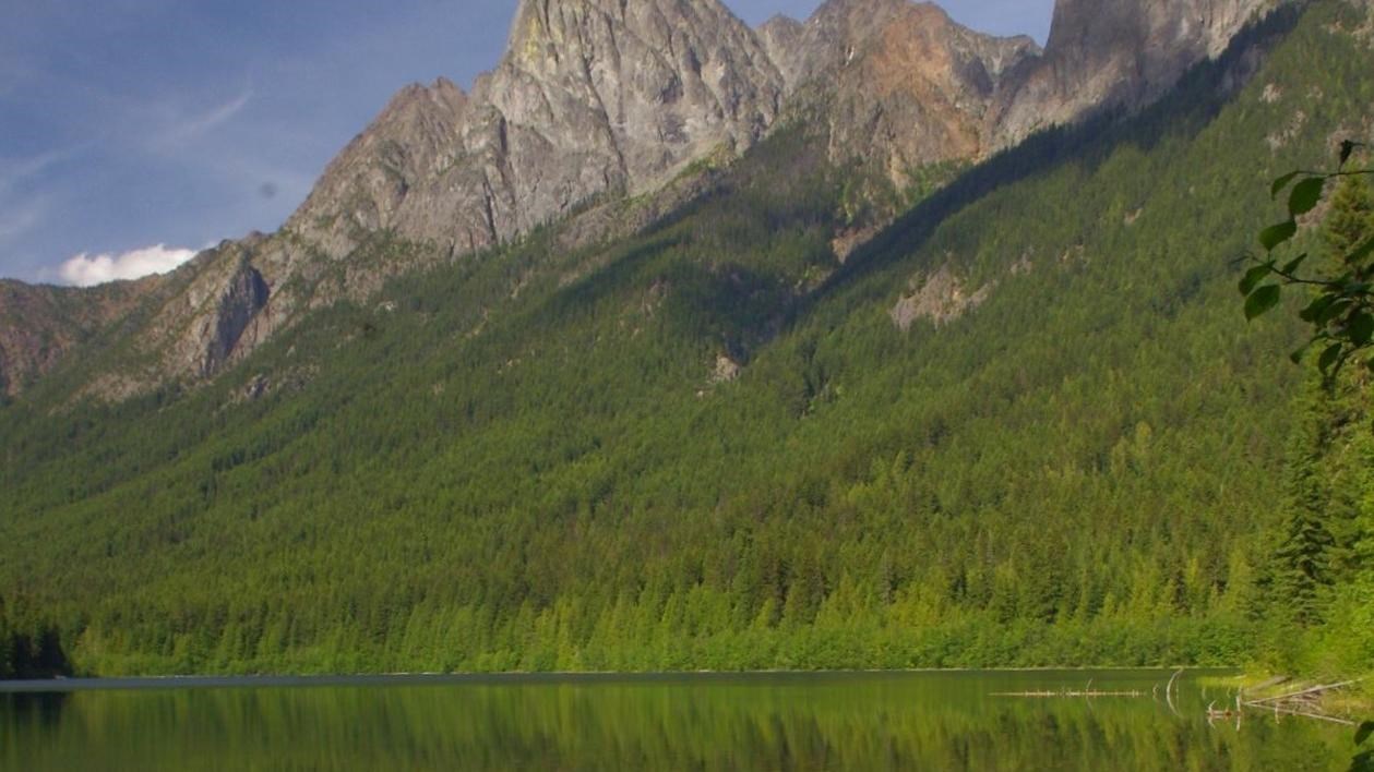 A clear blue lake in front on forested shores and a mountain.