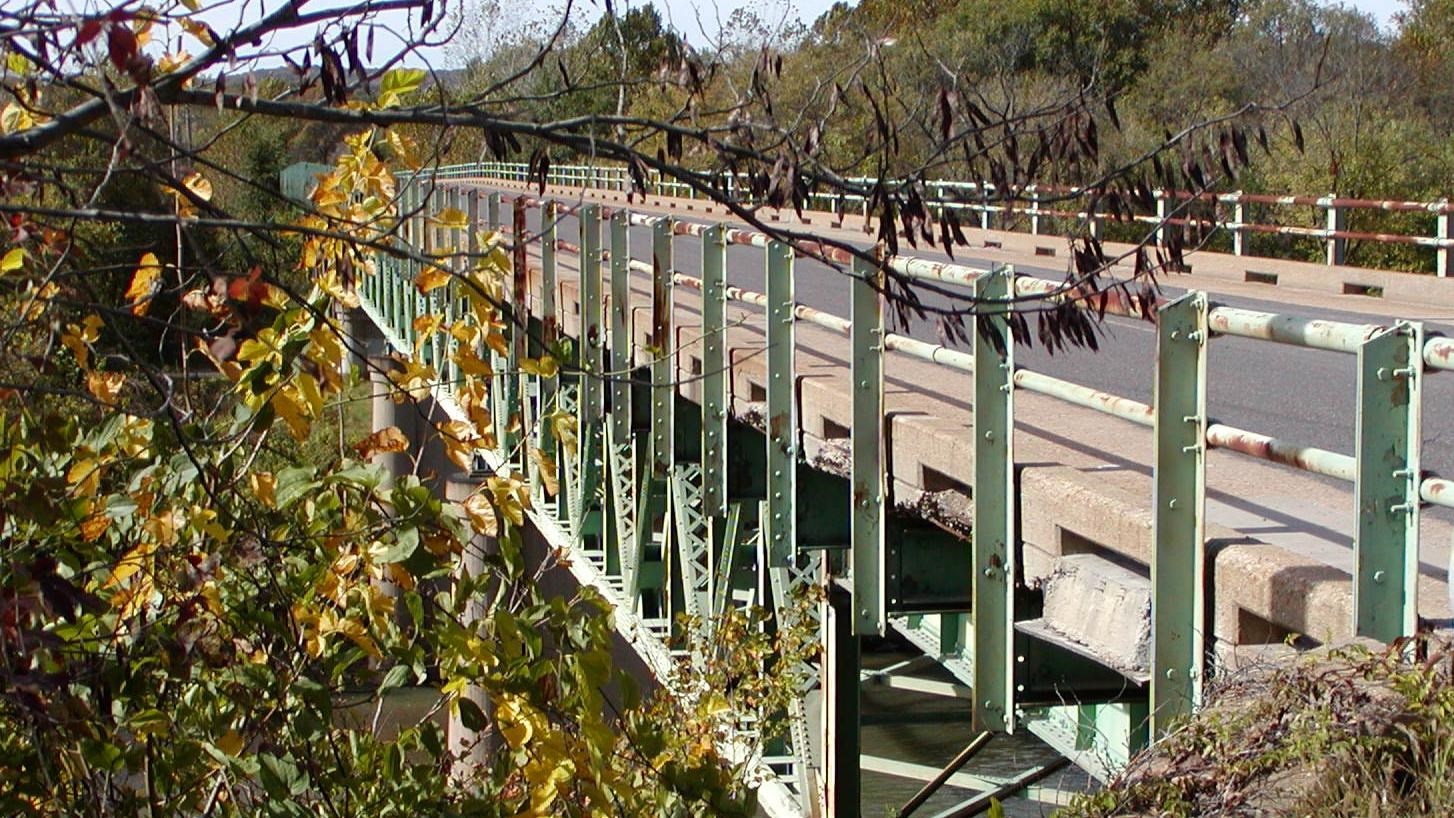 A large steel truss bridge across a river surrounded by green trees.