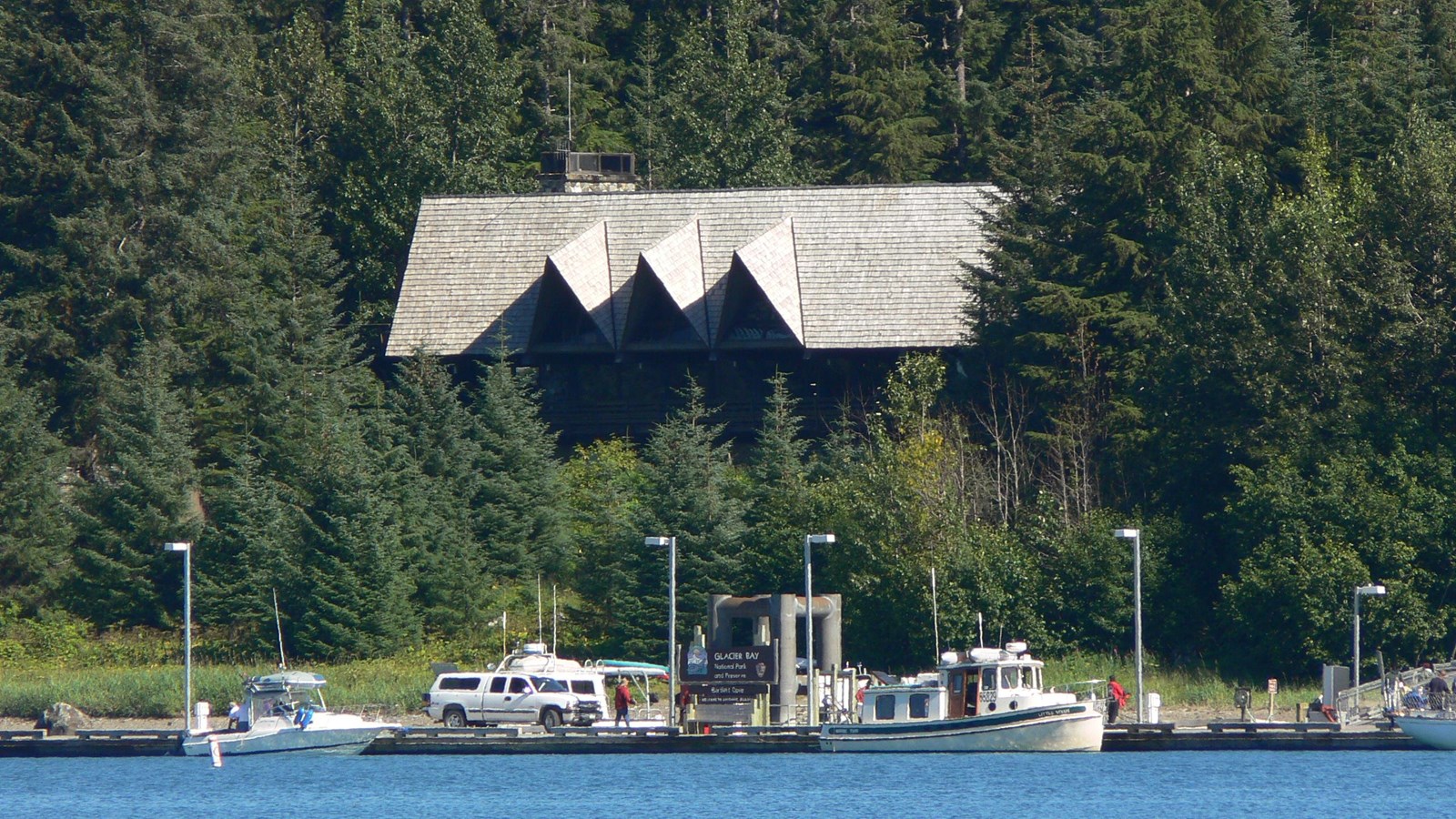 The glacier Bay lodge peeks above spruce trees in Bartlett Cove. Dock and boats in foreground