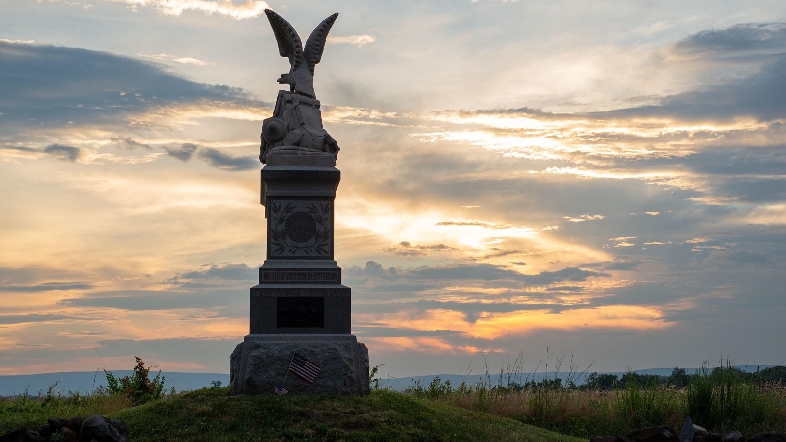 A monument with an eagle on top backlit by a sunset.