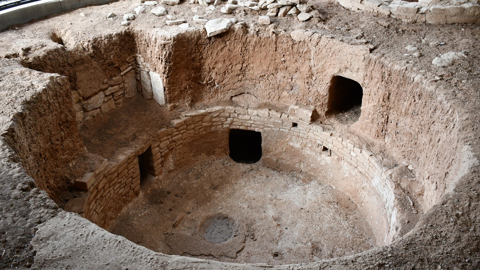 A kiva structure dug down into the earth with a fire pit and tunnel features.