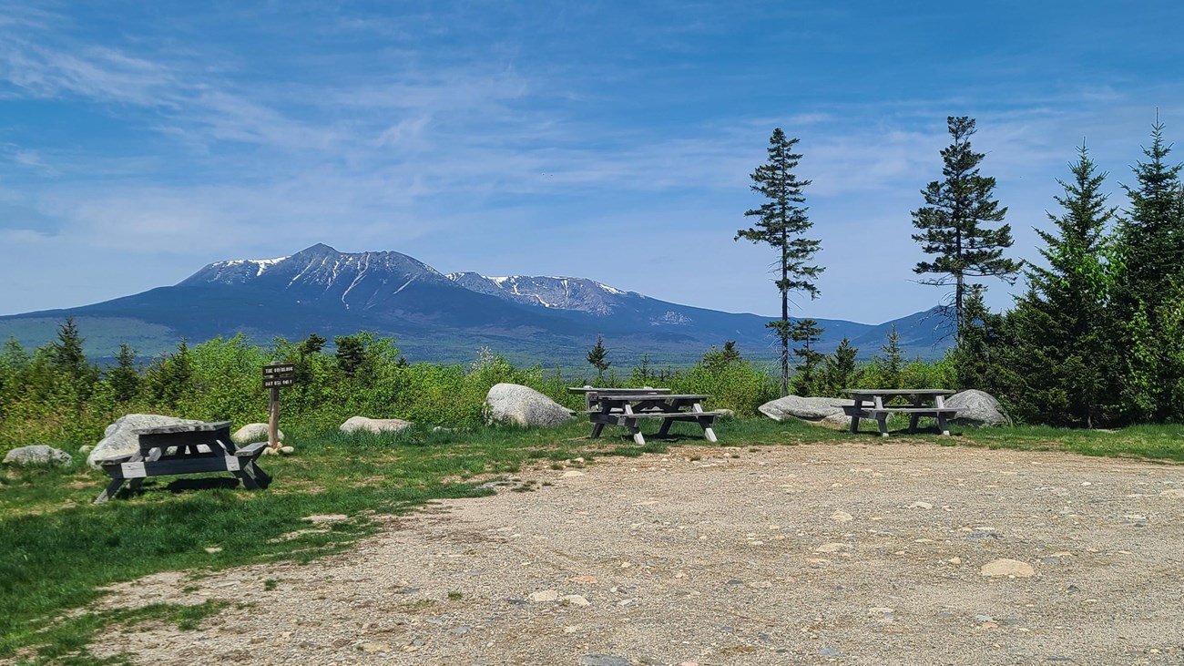Three picnic tables sit facing an expansive view of neighboring Katahdin on a sunny day.