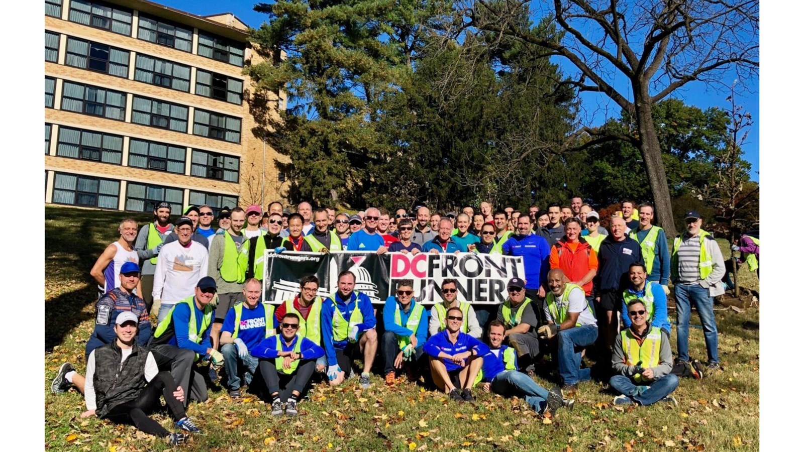 A large group of people in front of a grove of trees with a banner that reads 
