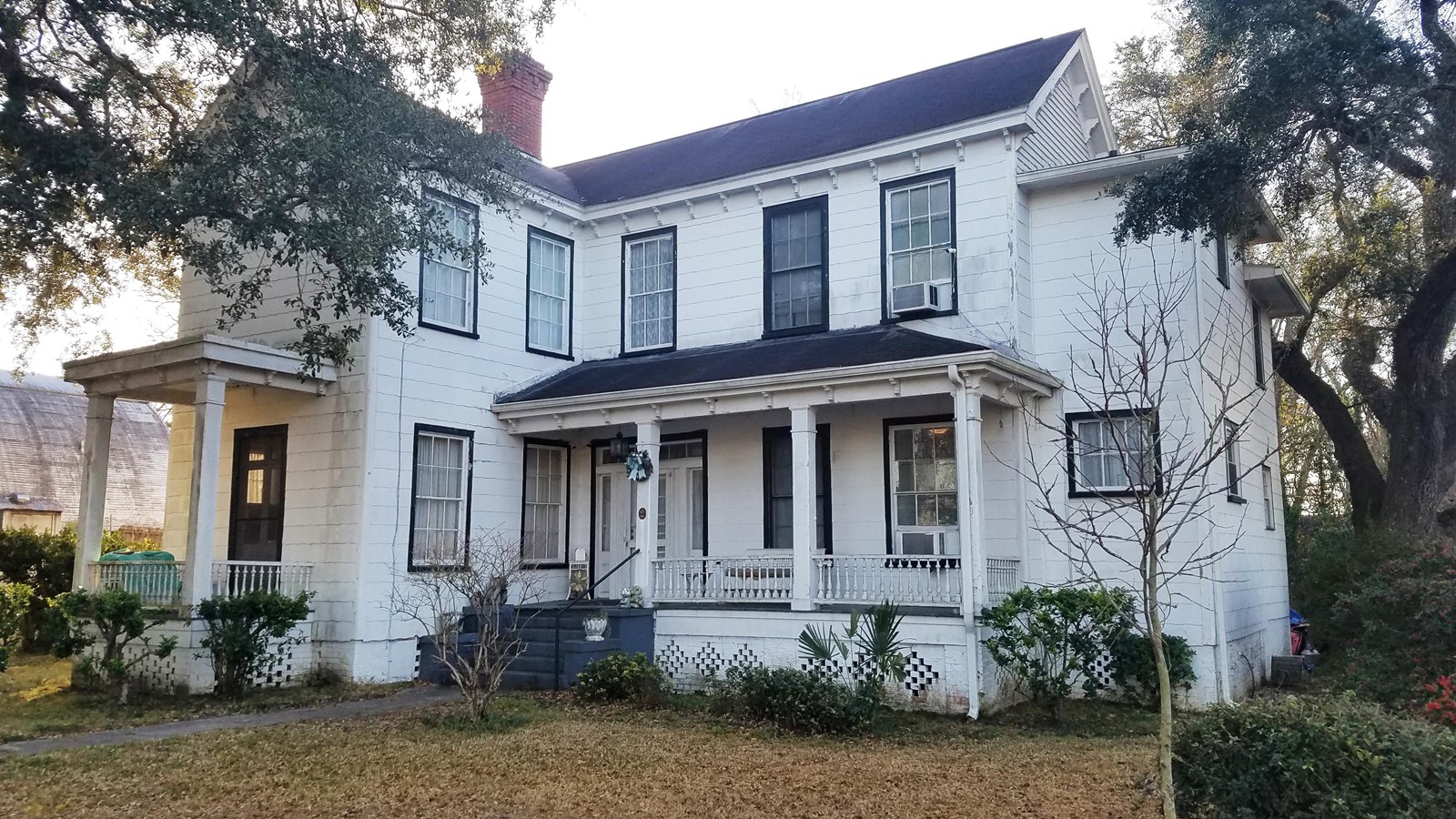 2 story white wooden home in an L shaped configuration and a few trees. 