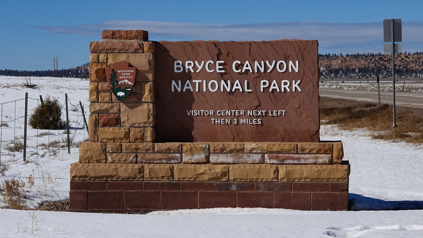 A stone monument sign of red rock reading Bryce Canyon National Park with an arrowhead sign