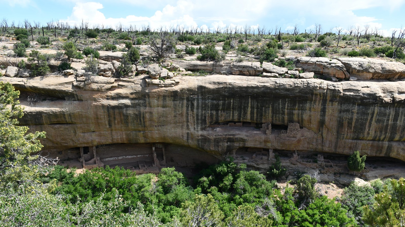A view of stone-built pueblo villages beneath a sandstone rock overhang.